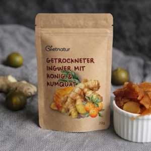 Getrocknete Ingwerstücke in einer Schale neben frischen Ingwerwurzeln und Kumquats